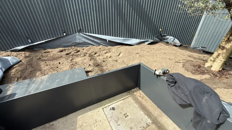 Een grote metalen plantenbak, geplaatst en met aarde gevuld.